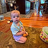 bucket, cabinet, carpet, child, curious, floor, hair_tie, home, indoor, kitchen, person, play, refrigerator, shorts, sitting, stove, toddler, toy, tshirt, wooden_floor