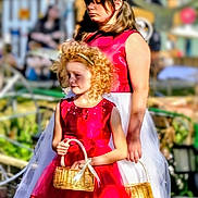 Stella is registered to the contest to win money with this photo: child, children, flower_girl, dress, red_dress, white_skirt, basket, curly_hair, blonde_hair, dark_hair, outdoor, garden, sunlight, grass, footwear, portrait, person, event, ceremony, holding