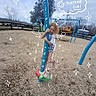Stella is registered to the contest to win money with this photo: child, playground, play_equipment, pole, wood_chips, outdoor, swing_set, tree, fence, cloudy_sky, curly_hair, white_clothing, pink_shoes, doodles, sparkles, date_stamp, fun, smiling, holding, park