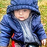 baby, child, hoodie, jacket, outdoor, grass, cold_weather, sitting, curious, young_child, winter_clothing, face, person, nature, playful, puffer_jacket, casual, seasonal, cute, exploration