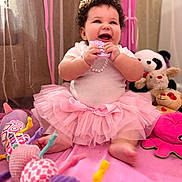 Sarai is registered to the contest to win money with this photo: baby, child, tutu, pink, curly_hair, smiling, toy, stuffed_animal, plush, indoor, blanket, cute, happy, playtime, girl, sitting, decor, soft_toys, infant, joyful