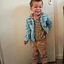 child, boy, smiling, curly_hair, denim_jacket, checkered_shirt, pants, boots, indoor, door, floor, standing, happy, casual_clothing, person, young, cute, fashion, portrait, full_body