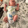 Hunner joined the competition — help win amazing prizes! baby, infant, onesie, dinosaur_print, white_socks, bed, quilt, floral_pattern, sleepwear, newborn, cute, resting, person, child, soft_lighting, indoors, portrait, small_hands, blanket, peaceful