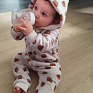 Lewis a rejoint le concours — aidez-le/la à gagner de superbes lots ! baby, child, bottle, onesie, hood, flooring, indoor, infant, cute, drinking, sitting, cozy, curly_hair, patterned_clothing, soft_texture, footwear_off, portrait, young_child, warm_clothing, home