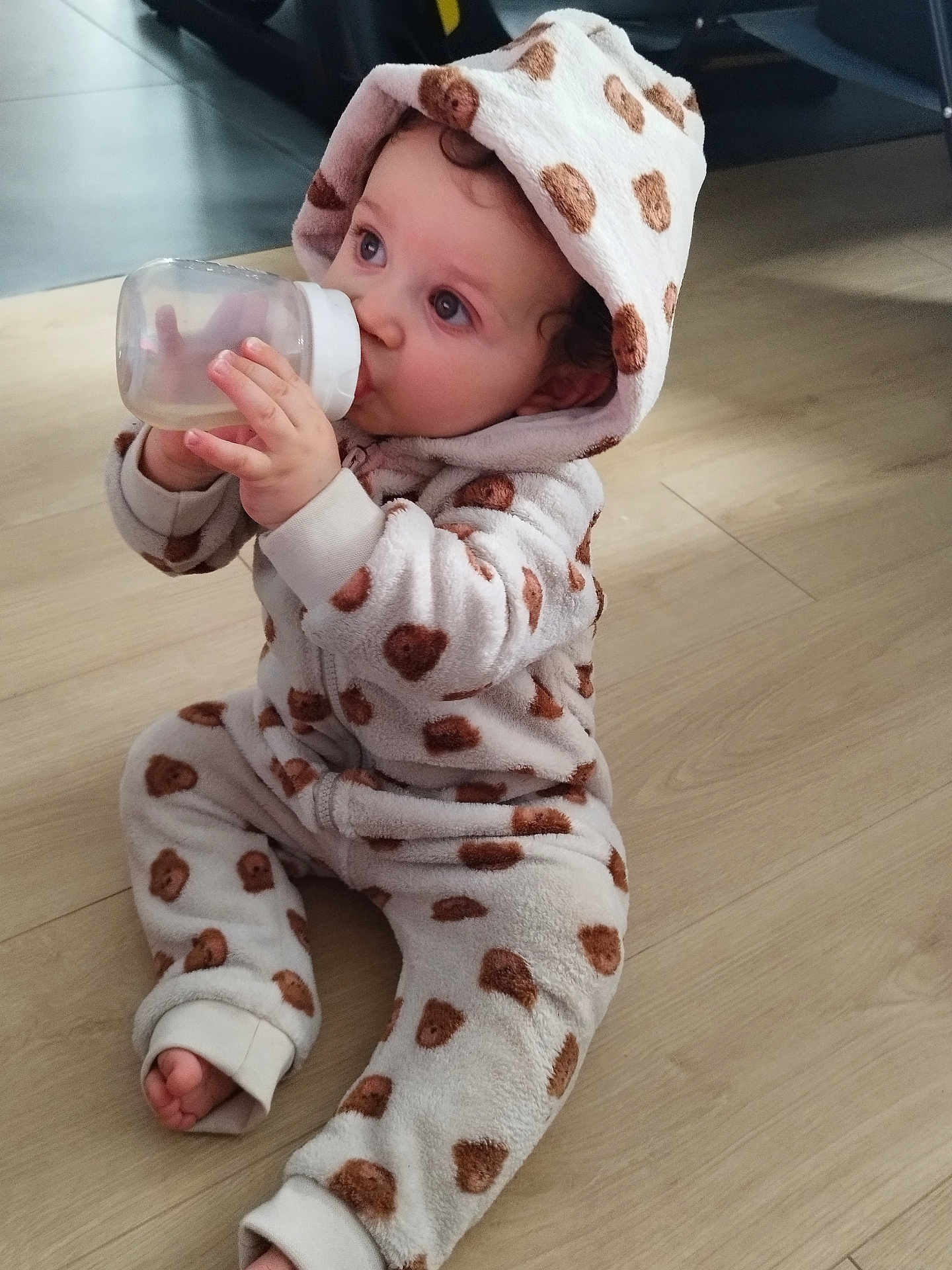 Lewis a rejoint le concours — aidez-le/la à gagner de superbes lots ! baby, child, bottle, onesie, hood, flooring, indoor, infant, cute, drinking, sitting, cozy, curly_hair, patterned_clothing, soft_texture, footwear_off, portrait, young_child, warm_clothing, home