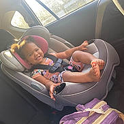 Octavia is registered to the contest to win money with this photo: toddler, child, car_seat, smile, happy, curly_hair, car_interior, sunlight, seatbelt, clothing, purple_backpack, window, safety, cute, baby, person, seat, transportation, daylight, casual