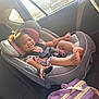 toddler, child, car_seat, smile, happy, curly_hair, car_interior, sunlight, seatbelt, clothing, purple_backpack, window, safety, cute, baby, person, seat, transportation, daylight, casual