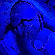 Fisher is registered to the contest to win money with this photo: baby, infant, pacifier, eye_mask, hand, blue_light, sleeping, bed, blanket, newborn, medical_tube, closeup, resting, comfort, soft_texture, child, peaceful, nursery, hospital, care