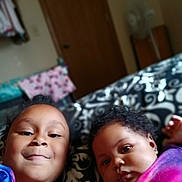 Za'Karrah is registered to the contest to win money with this photo: child, baby, bed, blanket, face, indoor, person, portrait, smile, curly_hair, clothing, room, door, fabric, pattern, furniture, young_child, sibling, cute, lying_down