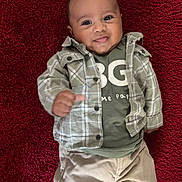 Léandro participe au concours pour gagner de l'argent avec cette photo : baby, infant, smiling, lying_down, red_rug, plaid_shirt, green_tshirt, pants, portrait, face, eyes, hand, skin, clothing, cute, adorable, brown_eyes, casual_outfit, indoor, closeup