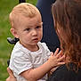 toddler, child, woman, outdoor, grass, curly_hair, blonde_hair, white_shirt, face, person, holding, baby, expression, portrait, hands, interaction, young_child, people, nature, casual
