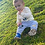 toddler, child, grass, outdoor, soccer_ball, yellow_building, blue_shoes, mickey_mouse, casual_clothing, sitting, finger_in_mouth, curious, sunlight, playing, nature, young_child, green_grass, daytime, person, sports_equipment