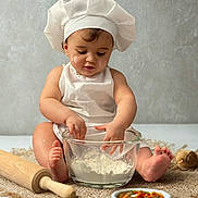 Eline participe au concours pour gagner de l'argent avec cette photo : baby, child, chef_hat, apron, flour, glass_bowl, rolling_pin, barefoot, sitting, cooking, kitchen, food, dough, cute, messy, infant, table, wooden_spoon, vegetables, homemade