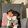 toddler, child, smiling, curly_hair, bow, gray_armchair, pink_pillow, plant, white_collar, gray_sweater, white_tights, happy, indoor, portrait, sitting, cozy, cute, baby, furniture, home