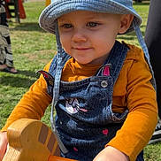 Shelby a rejoint le concours — aidez-le/la à gagner de superbes lots ! toddler, child, hat, bucket_hat, denim_overalls, cat_design, outdoor, playground, toy, wooden_toy, grass, yellow, orange, person, hand, face, cute, playing, sunny, day