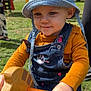 toddler, child, hat, bucket_hat, denim_overalls, cat_design, outdoor, playground, toy, wooden_toy, grass, yellow, orange, person, hand, face, cute, playing, sunny, day