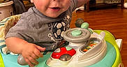 Mason is registered to the contest to win money with this photo: baby, car_toy, child, face, furniture, gray_shirt, hands, happy, head, indoor, living_room, person, playful, smiling, soccer_ball, toddler, toy, walker, wood_floor, young_child
