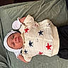 baby, infant, knit_sweater, stars, white_hat, mittens, green_blanket, lying_down, cute, peaceful, clothing, portrait, newborn, young_child, indoor, soft_texture, comfort, relaxation, child, person
