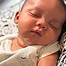 baby, sleeping, close_up, face, infant, peaceful, chubby_cheeks, soft_skin, white_clothing, patterned_background, portrait, indoors, cute, relaxed, child, newborn, resting, calm, human, skin