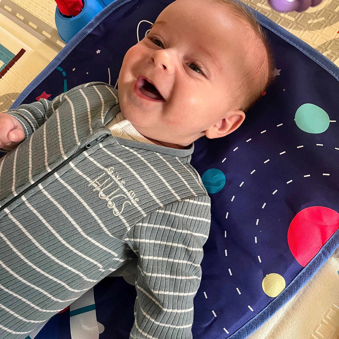 Valdek participe au concours pour gagner de l'argent avec cette photo : baby, cheerful, child, colorful, cute, expression, face, hand, happy, head, indoor, infant, lying_down, onesie, play_mat, smiling, space_theme, striped_clothing, toys, young
