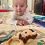 baby, infant, play_mat, toy, crochet_toy, lion_toy, pacifier, floor, indoors, child, cute, smiling, curious, person, lying_down, white_clothing, wooden_ring, home, carpet, soft_lighting