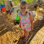 Addie is registered to the contest to win money with this photo: child, girl, smiling, cage, chickens, ribbons, award, sunlight, outdoor, fair, sand, woodchips, animal, poultry, footwear, colorful_clothing, hair_bow, happy, person, summer