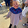 Addie is registered to the contest to win money with this photo: child, smile, face_paint, costume, outdoor, sidewalk, people, casual_clothing, shoes, brick_wall, sunlight, happy, person, black_pants, hat, purple_shirt, bag, shadow, young_child, playful