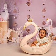 Romy participe au concours pour gagner de l'argent avec cette photo : toddler, child, swan, crown, seat, pink, decor, background, ornaments, feathers, cute, smiling, indoor, portrait, baby, soft_lighting, playful, props, studio, happiness