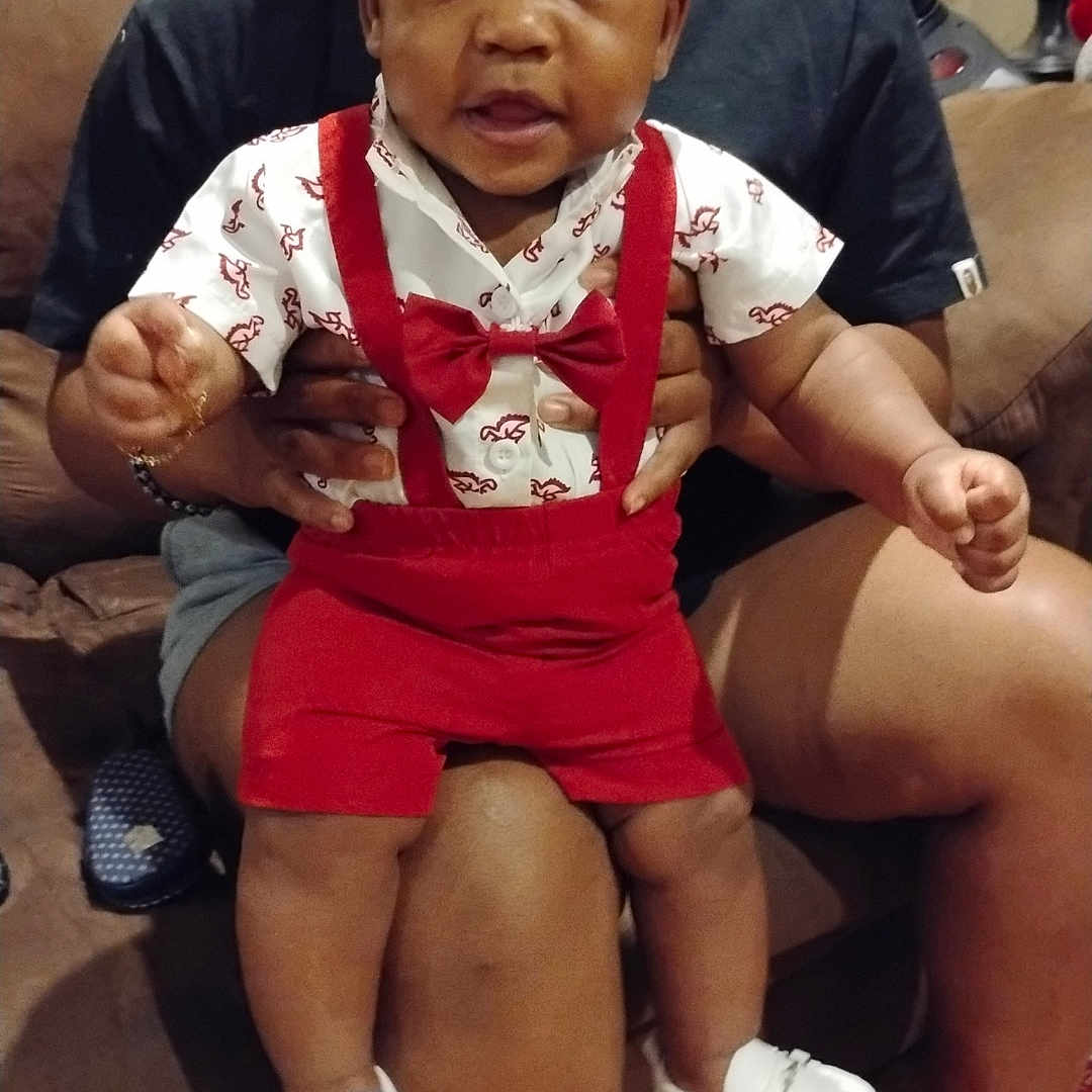 Jaheem joined the competition — help win amazing prizes! adult, baby, bow_tie, casual, child, clothing, couch, curious, family, hands, home, indoor, lamp, legs, person, red_suspender, seated, smiling, white_shoes, wooden_floor