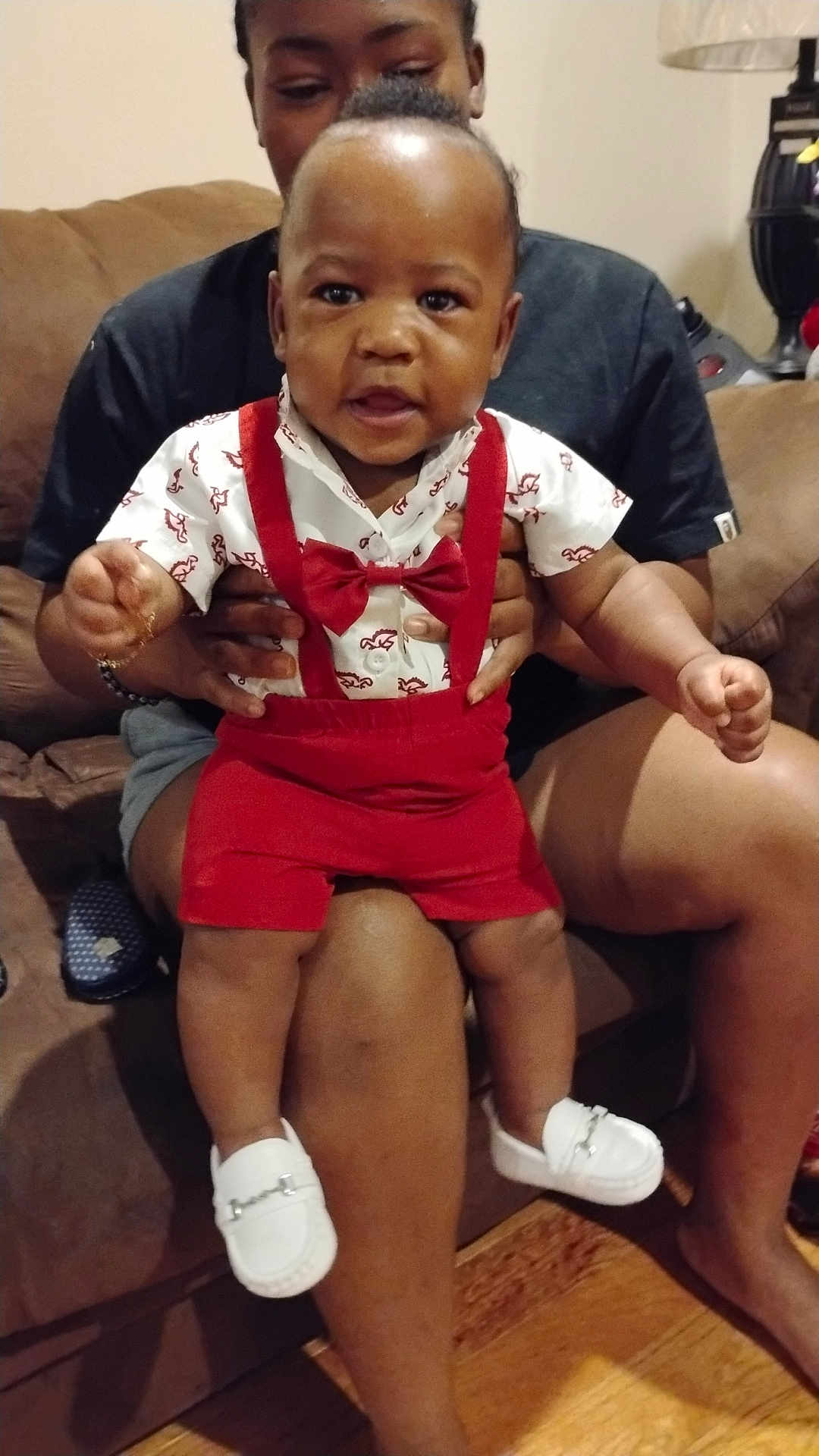 Jaheem joined the competition — help win amazing prizes! baby, child, person, adult, couch, indoor, clothing, red_suspender, bow_tie, white_shoes, legs, hands, wooden_floor, lamp, casual, seated, smiling, curious, home, family
