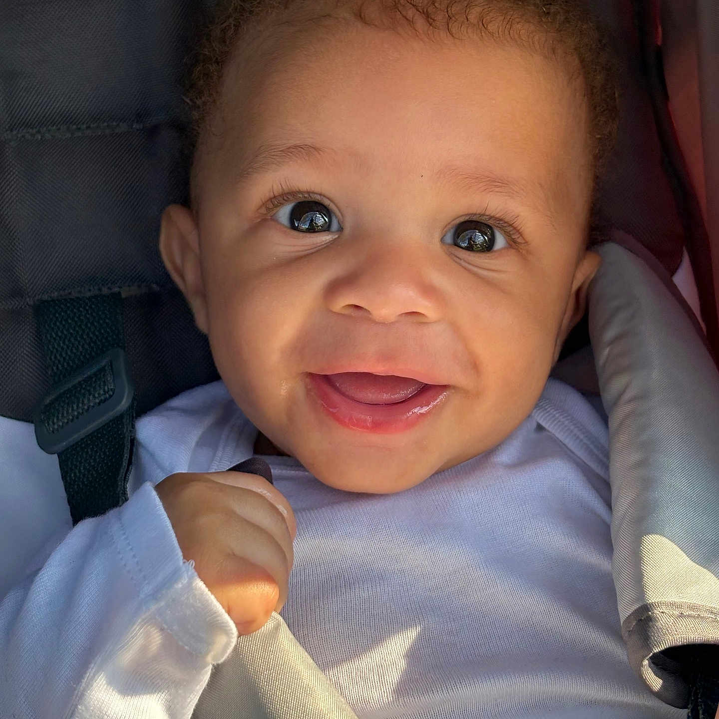 Kahmauri is registered to the contest to win money with this photo: baby, infant, smiling, face, eyes, clothing, white_shirt, car_seat, seat_belt, child, cute, happy, portrait, closeup, skin, hand, curly_hair, indoors, person, young