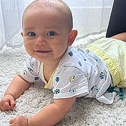 Léandre participe au concours pour gagner de l'argent avec cette photo : arms, baby, carpet, child, clothing, crawling, curtains, face, floor, happy, indoor, infant, natural_light, pants, patterned_clothing, person, smile, tshirt, white_carpet, window