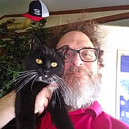 Mooch is registered to the contest to win money with this photo: beard, black_cat, casual, cat, cozy, facial_hair, feline, glasses, hat, indoor, man, pet, pipe, plant, portrait, red_shirt, selfie, smile, whiskers, yellow_eyes