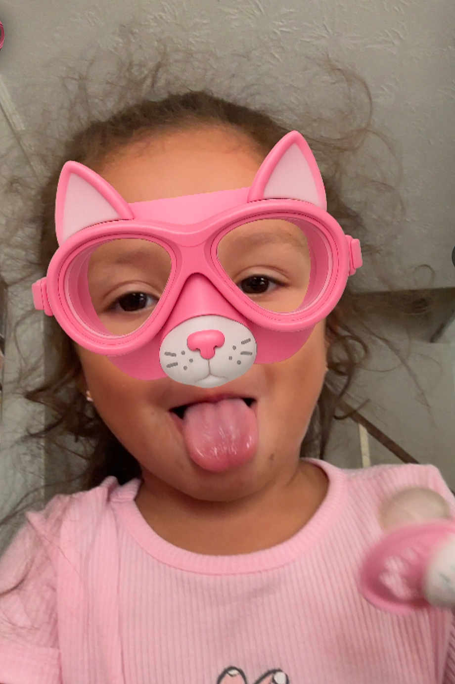 Nayeli joined the competition — help win amazing prizes! child, face, pink, glasses, virtual_filter, cat_ears, tongue_out, pacifier, indoor, curly_hair, playful, person, portrait, silly_face, young, cute, pink_shirt, fun, expression, headshot