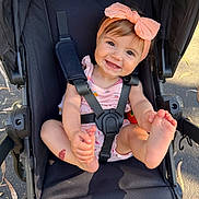 Makenzie is registered to the contest to win money with this photo: baby, infant, stroller, headband, bow, smile, toes, hands, safety_harness, seat, outdoor, sunlight, cute, pink_clothing, happy, portrait, pavement, leaf, child, playful