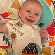 Archie is registered to the contest to win money with this photo: baby, smiling, play_mat, colorful, bib, toy, infant, happy, face, child, cute, indoor, closeup, polka_dot, music_notes, hand, blue_eyes, fabric, pattern, soft_toys