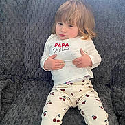 Athéna participe au concours pour gagner de l'argent avec cette photo : child, toddler, sitting, couch, clothing, pants, shirt, face, hair, indoor, expression, pattern, cherry, white_shirt, text_on_clothing, relaxed, furniture, cute, portrait, cozy