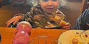 Mason joined the competition — help win amazing prizes! toddler, child, curly_hair, camouflage_shirt, restaurant, table, bread, sippy_cup, plate, food, napkin, basket, chair, window, indoor, person, eating, meal, happy, casual