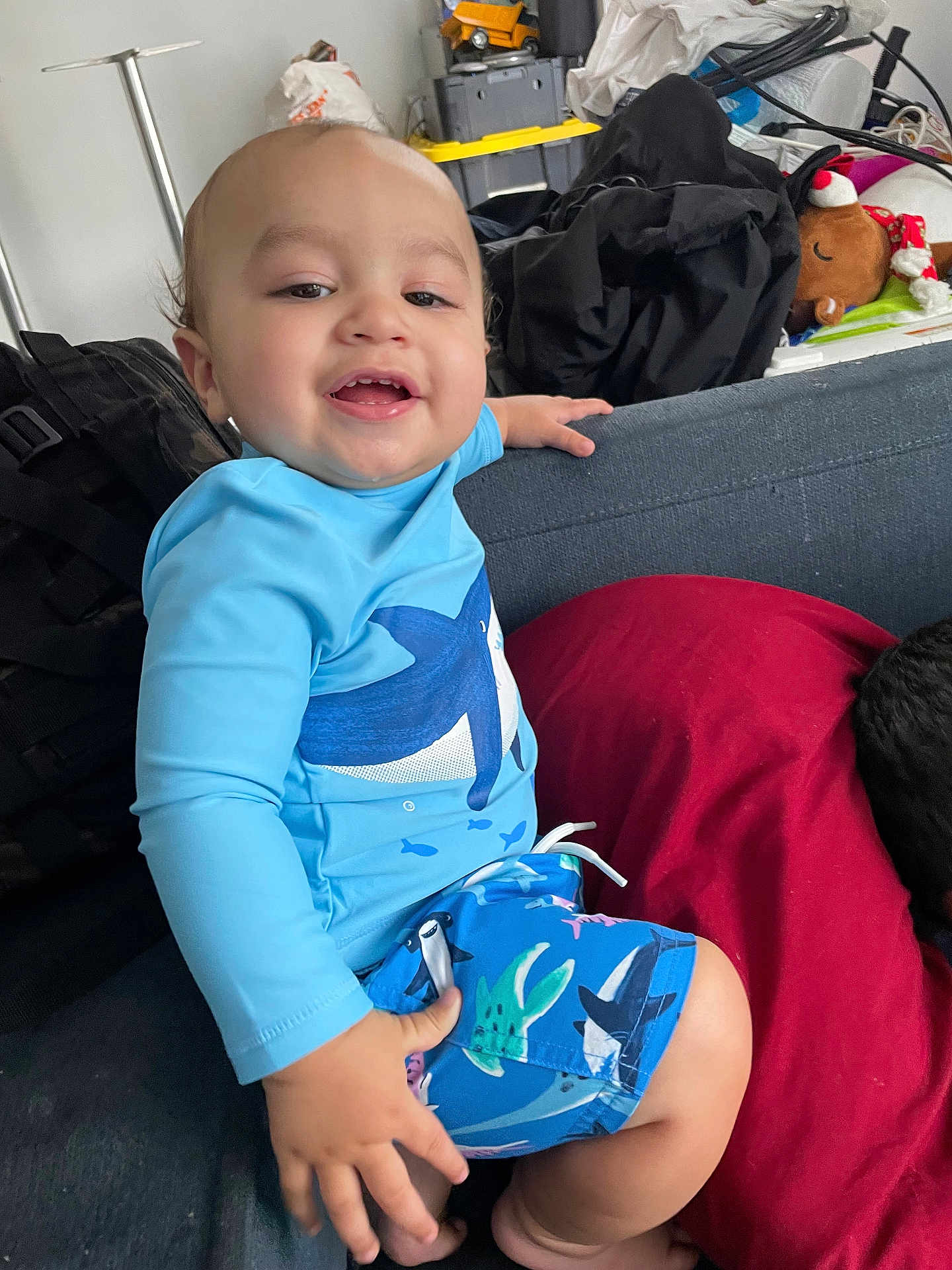 Mason joined the competition — help win amazing prizes! toddler, child, smiling, blue_clothing, shark_design, shorts, long_sleeve_shirt, couch, red_pillow, indoor, happy, baby, person, face, hand, foot, living_room, toy, casual, home