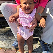 Raji joined the competition — help win amazing prizes! baby, child, smile, outdoors, bench, adult_hands, pink_outfit, sneakers, legs, concrete, park, sunlight, happy, portrait, toddler, holding, ruffled_dress, family, person, joyful