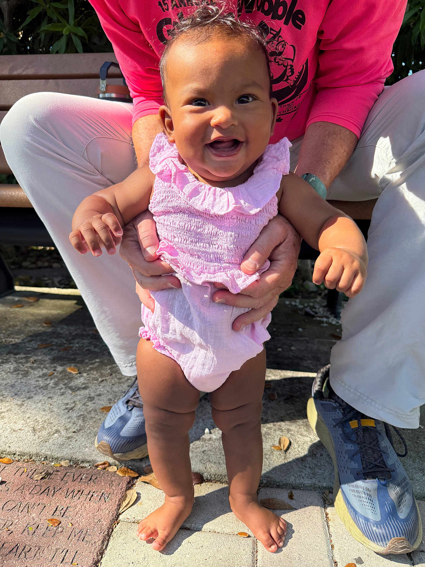 Raji joined the competition — help win amazing prizes! baby, child, smile, outdoors, bench, adult_hands, pink_outfit, sneakers, legs, concrete, park, sunlight, happy, portrait, toddler, holding, ruffled_dress, family, person, joyful