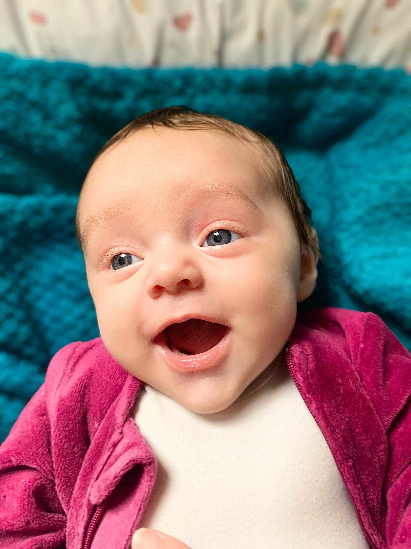 Margaux participe au concours pour gagner de l'argent avec cette photo : baby, infant, smiling, face, blue_eyes, open_mouth, clothing, jacket, pink, purple, teal, knitted_blanket, background, portrait, cute, happy, skin, human, closeup, indoor