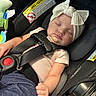 baby, infant, sleeping, car_seat, seatbelt, harness, bow_headband, pink_clothing, portrait, face, closed_eyes, indoors, vehicle, automobile, safety, buckle, red_button, soft_lighting, peaceful, newborn