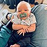 baby, pacifier, infant, person, clothing, shirt, pants, hand, foot, lap, indoor, shoe, furniture, relaxation, casual, comfort, closeup, portrait, child, human