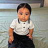 child, toddler, baby, portrait, sitting, indoors, bed, bedding, white_shirt, black_pants, collared_shirt, fashion, straight_hair, dark_hair, brown_eyes, serious_expression, camera_facing, person, close_up, home
