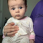 Luna is registered to the contest to win money with this photo: adult, baby, child, clothing, curious, door, expression, eyes, face, fingernails, hand, holding, home, indoor, infant, onesie, person, portrait, purple_shirt, skin