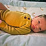 baby, blanket, calm, child, clothing, cute, face, head, indoors, infant, lying_down, newborn, person, portrait, rainbow_pattern, resting, skin, sleepwear, soft_texture, yellow_onesie