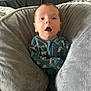 animal_print, baby, blanket, child, comfortable, cozy, face, grey, head, indoor, infant, mouth_open, newborn, onesie, person, plush_pillow, seated, soft_texture, surprised_expression, wide_eyes