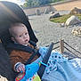 baby, stroller, toy, blanket, outdoor, child, sunlight, grass, rocks, garden, nature, blue_eyes, clothing, hand, face, person, portrait, seatbelt, fabric, peaceful