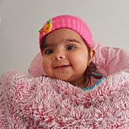 Shanaya is registered to the contest to win money with this photo: baby, child, infant, smiling, portrait, pink_hat, flower, blanket, fuzzy_blanket, sitting, indoors, close_up, face, eyes, cheeks, clothing, cozy, happy, social_media_screenshot, phone_interface